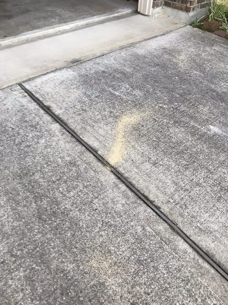 Yellowish granular treatment spread on a concrete walkway beside a home foundation and expansion joint