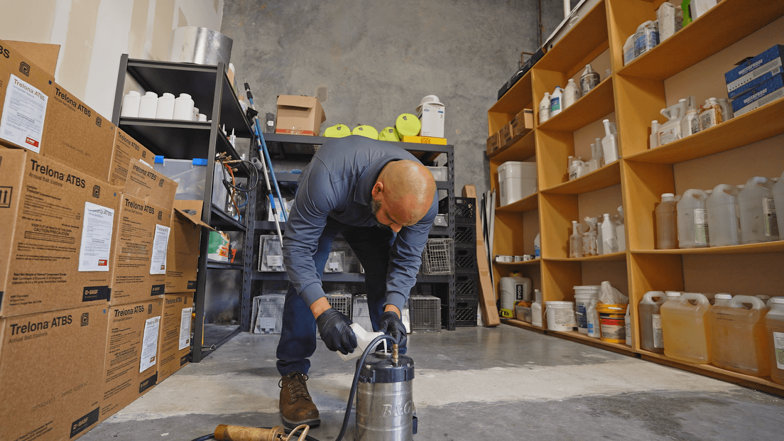 Technician wearing protective gloves pouring a liquid lawn treatment into a stainless-steel compressed-air sprayer